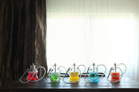 Several colorful arranged hookahs on a wooden table with a window in the background.の写真素材
