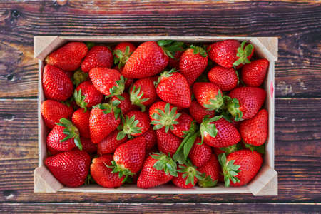 Deep red strawberries picked in a farmer wooden box on dark colored wooden tableの写真素材