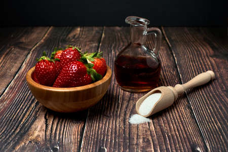 Wooden bowl with fresh red strawberries fresh with sugar and vinegar for its preparation on a black backgroundの写真素材
