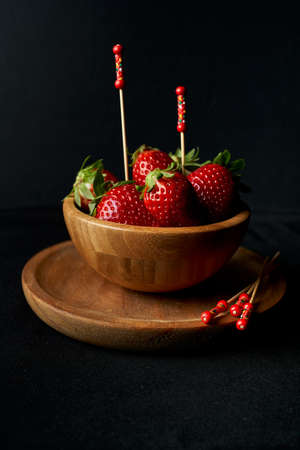 Wooden bowl with fresh red strawberries inside decorated with decorative chopsticks on a black backgroundの写真素材
