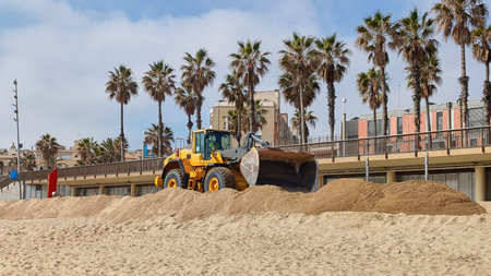 Excavator and dump truck working on beach restoration and sand replenishment on an urban beach in...
