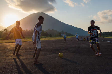 Teenagers play football on the airstrip of Bandaneira with the volcano in the backgroundのeditorial素材