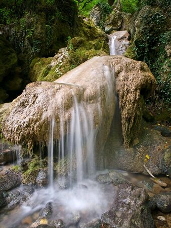 Small waterfall running from rock in shadow forestの写真素材