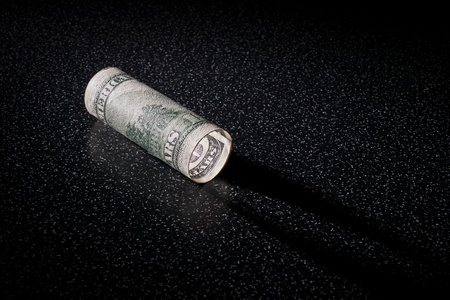 American 100 dollars greenback rolled like a lantern lies on the blackの写真素材