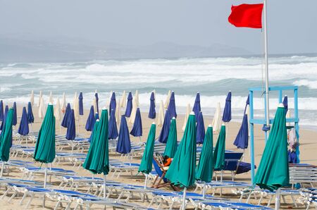 Summer end. Closed umbrellas, closed beach loungers , stormy sea and red flag. No bathers, bathing prohibitedの写真素材