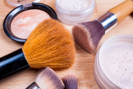 Face makeup cosmetics on a light wooden floor - brush, powder, blush, foundation.
