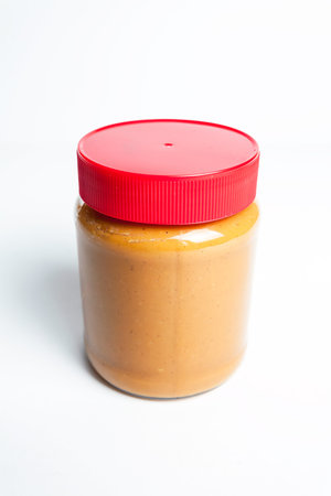 Peanut butter in a jar with red cap isolated on a white background.