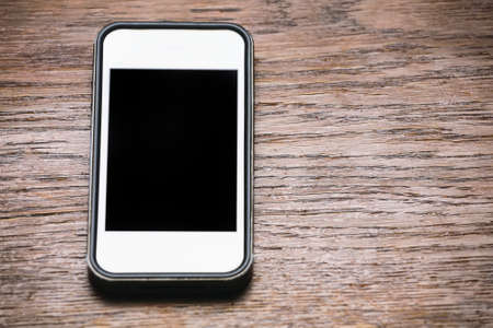 Vintage dark wood background white phone with black screen.の写真素材