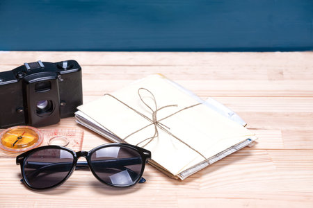 Sunglasses, compass, old film camera and a bunch of letters on a light and blue wooden background....