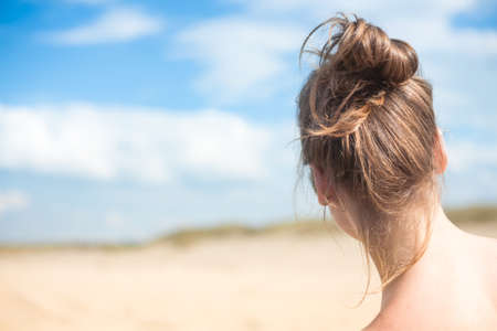 Beautiful young woman on a sandy beach with blue sky. back viewの写真素材