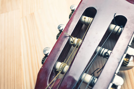 Head and pegs of a guitar on a light wooden background. Musical instrument. Vintage colors. Copy...