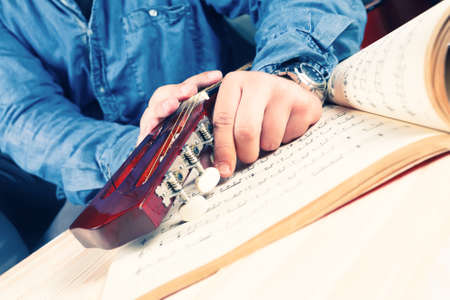 Young man tuning a guitar. Head, pegs and music notes. Vintage colors. Jeans shirt.の写真素材