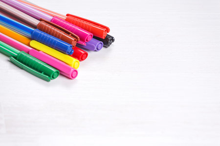 Colorful pens on natural white wooden background. Arranged in a stack. Copy space to the right.