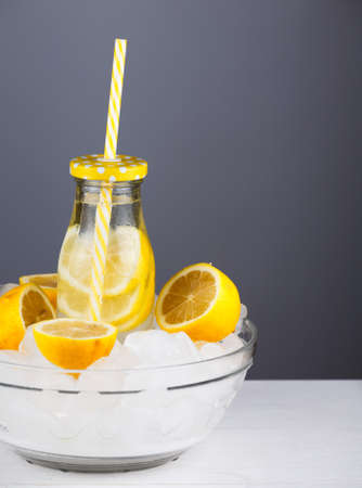 Lemonade drink in trendy bottle with straw in a bowl full of ice. Copy space to the right. Bunch of lemon halves. Abstract of summer holiday refreshment beverage.の写真素材