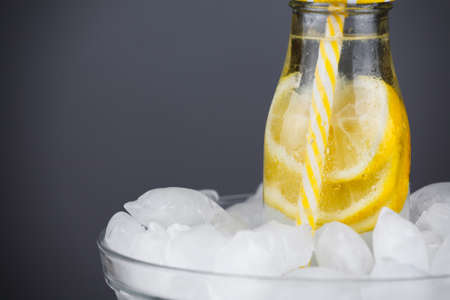 Lemonade drink in trendy bottle with straw on ice. Concept of summer beverage refreshment. Copy space to the left.の写真素材