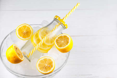 Lemonade drink in trendy bottle with straw on ice. Copy space to the right. Bunch of lemons. Bright, vibrant colors.の写真素材