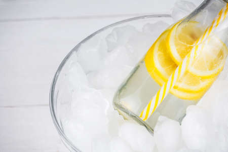 Lemonade drink in trendy bottle with straw on ice. Copy space to the left. Bunch of lemon slices.の写真素材