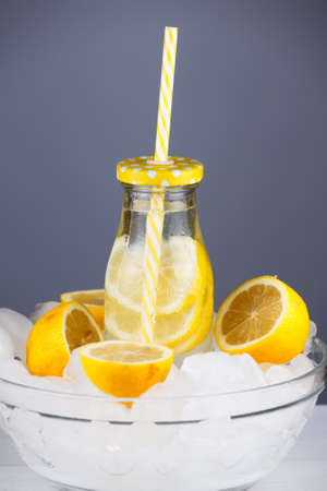 Lemonade drink in trendy bottle with straw in a bowl full of ice. Bunch of lemon halves. Concept of summer holiday beverage.の写真素材