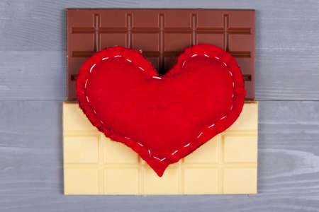 Red homemade heart on top of white and milk chocolate on grey background. Love of sweets and yin and yang concept.の写真素材