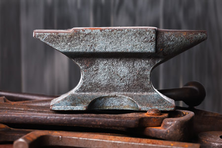Old rusty rugged anvil on top of other blacksmith tools on black wooden background.の写真素材