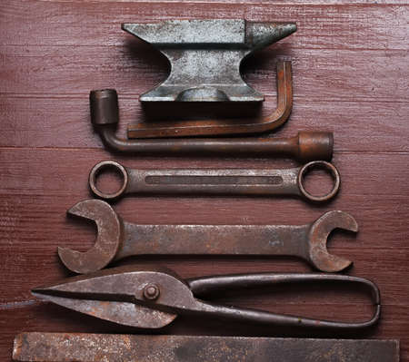 Old rusty rugged anvil and other blacksmith tools on brown natural wooden background in a shape of christmas tree. Flat lay top view.の写真素材