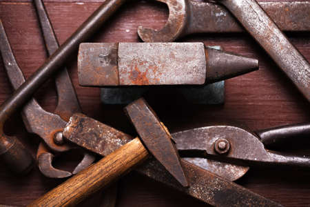 Old rusty rugged anvil and other blacksmith tools on brown natural wooden background. Flat lay top view.の写真素材