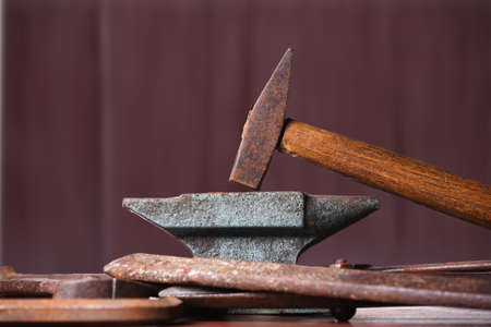 Old rusty rugged anvil, hammer and other blacksmith tools on brown natural wooden background.の写真素材