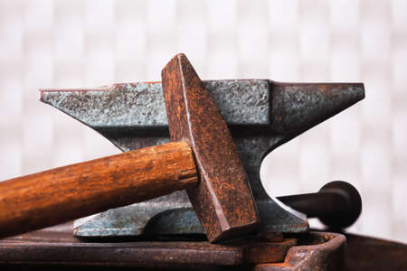 Old rusty rugged anvil with hammer on white checkered background.の写真素材