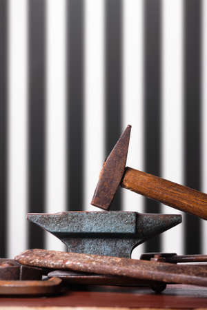 Old rusty rugged anvil, hammer and other blacksmith tools on striped black and white background.の写真素材