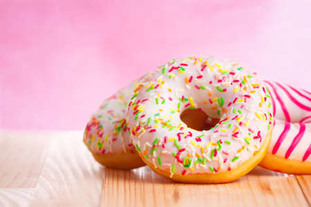 Colorful donuts on natural wooden table and pink background. Copy space to the left.の写真素材
