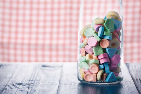 Colorful sweet candy in wine carafe on old wooden table against vintage kitchen dishcloth.の写真素材