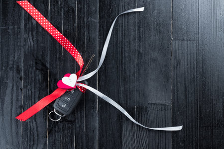 Cark key with a red ribbon adn a heart on black wooden table. Giving present or gift for valentine's day or christmas.の写真素材