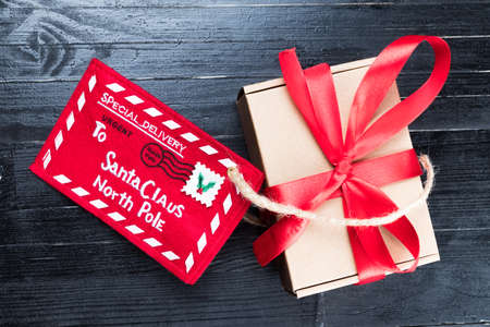 Red Letter to Santa Claus with paper box with ribbon bow on black natural wooden table. Christmas gift or present child fantasy concept.の写真素材