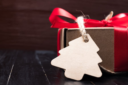 Pine tree label with twine attached on paper present with red ribbon bow. Black natural wooden...