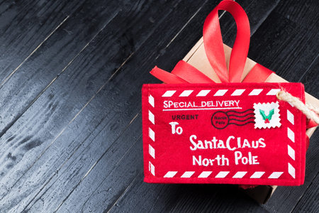 Red Letter to Santa Claus with paper box with ribbon bow on black natural wooden table. Christmas...