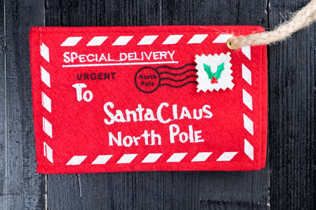 Red letter to Santa Claus envelope with jute twine attached on black natural wooden table. Christmas kid fantasy abstract concept.の写真素材