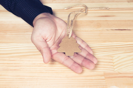 Elegant man or businessman hand holding pine tree shaped label with twine attached. Flat lay top...