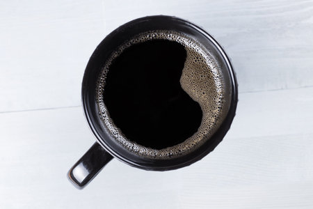 Black modern cup of coffee on gray natural wooden background.