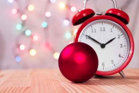 Tree bauble ornament with red vintage clock. Natural wooden table. Christmas lights bokeh...