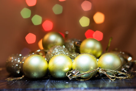 Yellow christmas tree baubles on black wooden table. Colorful lights bokeh background.