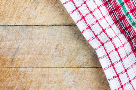 Christmas colored kitchen towel on old rugged natural wooden cutting board. Flat lay top view. Copy...