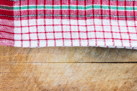 Christmas colored kitchen towel on old rugged natural wooden cutting board. Flat lay top view. Copy...