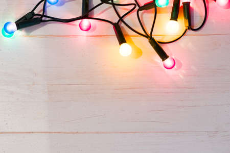 Colorful christmas tree lights on white natural wooden table. Copy space at the bottom. Flat lay top view.の写真素材