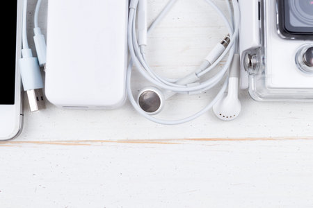 White technology on natural wooden table background. Power bank, cable, headphones, action camera,...