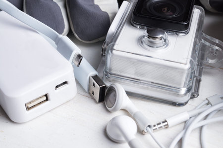 White technology on natural wooden table background. Power bank, action camera, head phones, cable,...
