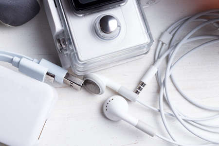 White technology on natural wooden table background. Power bank, action camera, head phones, cable. Active winter leisure time sports holidays abstract concept.の写真素材