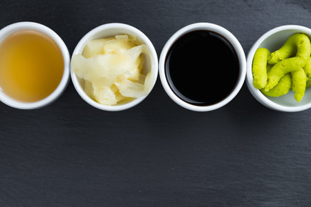 Ginger, Japanese horseradish wasabi, soy and fish sauce in small white bowls on black kitchen slate...
