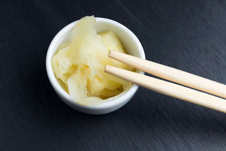 Ginger in small white bowl with chopsticks on black kitchen slate plate. Asian cuisine abstract concept.の写真素材