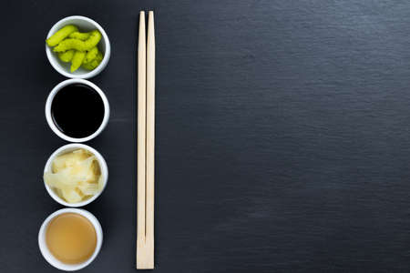 Soy and fish sauce, ginger, japanese horseradish wasabi in small white bowls with chopsticks on black kitchen slate plate background. Typical asian cuisine spices. Copy space on the right.の写真素材