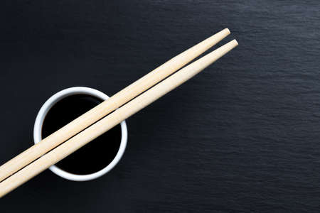 Soy sauce in small white bowl with chopsticks on black kitchen slate plate. Typical asian cuisine spice. Copy space on the right.の写真素材